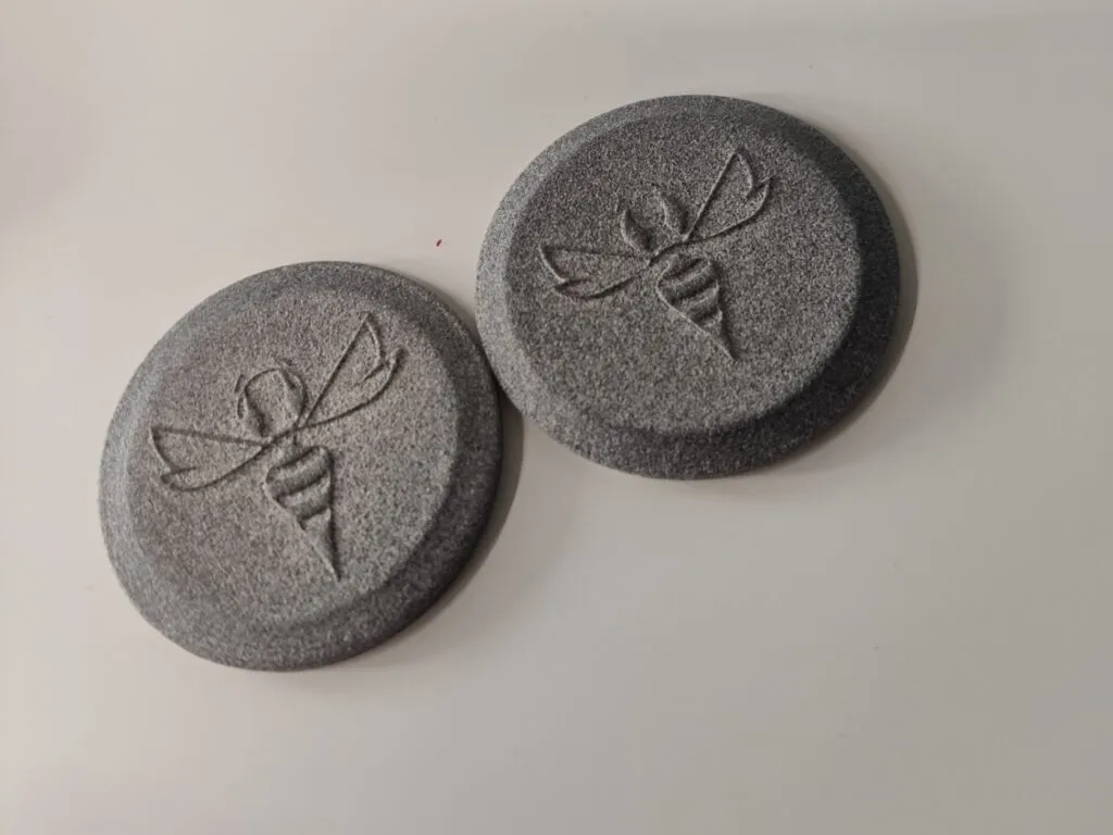 Two grey textured watch case elements with an embossed bee motif, 3D printed as a prototype for a custom personalized watch.
